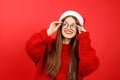 Young dreamy woman is waiting for a Christmas surprise, a girl in a Santa hat on a red background Royalty Free Stock Photo