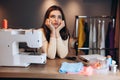 Young dressmaker woman sews clothes on sewing machine. Dreaming and wondering about something seamstress in workshop Royalty Free Stock Photo