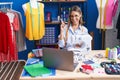 Young dressmaker woman using sewing machine smiling happy pointing with hand and finger to the side Royalty Free Stock Photo