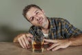 Young drunk and alcoholic man wasted drinking whiskey glass intoxicated and messy on dark background in alcohol ab