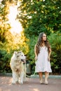 Young dwarf woman leads on a leash Malamute dog in park