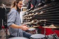 Young earded hipster sit close to drums and cumbals and playing on them. He hold two drum sticks in hands. Guy keeps Royalty Free Stock Photo