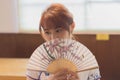 Young East Asian woman posing with an ornate oriental-style fan in front of her face.