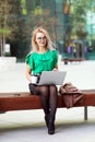 Young eastern European businesswoman walking on laptop on coffee break outside office building in windy day.