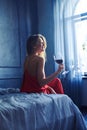 Young elated woman with glass of red wine sitting on the bed