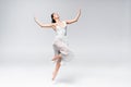 Elegant ballerina in white dress dancing on grey background