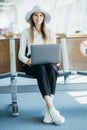 Young elegant business woman with hand luggage in international airport terminal, working on her laptop while waiting Royalty Free Stock Photo