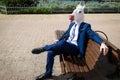 Young elegant man in funny mask and suit have a break in park Royalty Free Stock Photo
