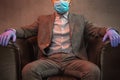 Young elegant man sits in a leather armchair with mask on his face and medical gloves