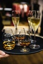 Young elegant man standing in the restaurant, holding a plate with glasses of wine and cognac, whisky. Man`s style Royalty Free Stock Photo