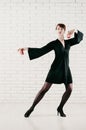 a young attractive woman in black dress, dancing with red castanets, white brick background