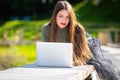 Young elegant woman in eyeglasses lying on bench in park and working on laptop on a sunny and windy day Royalty Free Stock Photo