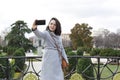 Young elegant woman sightseeing. She is taking a picture with her mobile phone of herself in a city garden Royalty Free Stock Photo