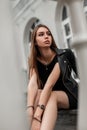 Young elegant woman in stylish black clothes sits on the steps in the city near a white building. Beautiful fashionable girl Royalty Free Stock Photo