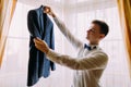 Young ellegant looking man holding out his jacket in a hotel room, preparing to dressing for an event Royalty Free Stock Photo