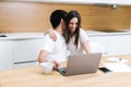 Young embracing couple is using laptop computer sitting on kitchen at home Royalty Free Stock Photo