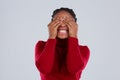 An emotional African-American girl covered eyes with hands and clenched her teeth. Gray background.