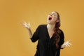 The young emotional angry woman screaming on gold studio background