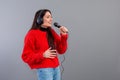 Young, emotional brunette with headphones and a microphone dressed in a red sweater sings karaoke