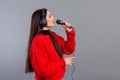 Young, emotional brunette with headphones and a microphone dressed in a red sweater sings karaoke