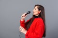 young, emotional brunette with a microphone dressed in a red sweater sings karaoke or says a speech