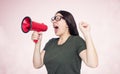 Young emotional girl with glasses shouts into a red megaphone, on light background. Woman protests