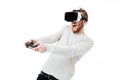 Young emotional man using virtual reality glasses and playing video game on white background. Boy with joystick in hands