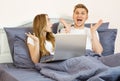 Young emotional married couple lying on bed at home and using laptop. Cheerful couple using a computer lying on their bed at home Royalty Free Stock Photo