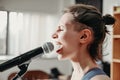 young emotional woman singing into a microphone. female rock singer on a rehearsal in record studio. side view Royalty Free Stock Photo