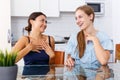 Young emotional women friends chatting and sharing secrets at table at home