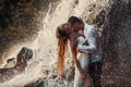 Young enamored couple hugs and kisses under spray of waterfall. Royalty Free Stock Photo