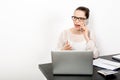 A young enerpreneur woman sits at her workplace with a laptop near a white wall while talking emotionally and loudly on the phone Royalty Free Stock Photo