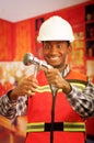 Young engineer wearing square pattern flanel shirt with red safety vest, holding showerhead and pliars smiling to camera