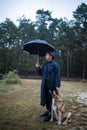 English man in stylish vintage coat and black hat walking in rainy forest with a dog. Royalty Free Stock Photo