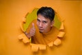 Young entertaining man through torn yellow paper hole showing thump up with facetious of content and happiness Royalty Free Stock Photo