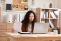 Young entrepreneur using laptop looking notes paper at home office desk.business asian woman professional work on computer Royalty Free Stock Photo