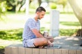 Young entrepreneur working at the park outside on wooden bench. Man using laptop, writing text. Street view. Concept of co-working Royalty Free Stock Photo