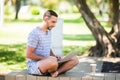 Young entrepreneur working at the park outside on wooden bench. Man using laptop, writing text. Street view. Concept of co-working Royalty Free Stock Photo