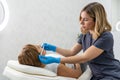 young esthetician measures with pen face of old woman lying at clinic