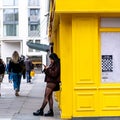 Young Ethnic Woman Leaning Against Yellow Building Using Mobile Phone