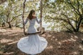 Young European beautiful girl in white bridal marriage dress posing on swing in forest trees on the ocean sea beach Royalty Free Stock Photo