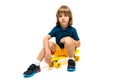 Young european cute child in sportswear sitting on a yellow skateboard on a white background