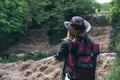 Young european female tourist with backpack and cowboy hat looking at the river washed away the bridge, the crossing was