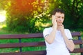 A young European guy in a white T-shirt speaks on the phone and sits on a bench in the city park. The concept of solving problems, Royalty Free Stock Photo