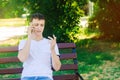 A young European guy in a white T-shirt speaks on the phone and sits on a bench in the city park. The man looks at his fingers, pu Royalty Free Stock Photo