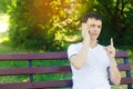 A young European guy in a white T-shirt speaks on the phone and sits on a bench in the city park and points with your finger. The Royalty Free Stock Photo