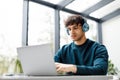 Young european male designer listening music on headphones while working on laptop at a desk in modern glass office Royalty Free Stock Photo