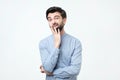 Young european man in blue shirt thinks, looks through incredulously