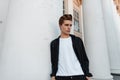 Young European man with a stylish hairstyle in an elegant black shirt in a white T-shirt is resting near a vintage building Royalty Free Stock Photo