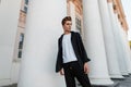 Young European man with a stylish hairstyle in a shirt in a t-shirt in striped pants is standing near a vintage white building Royalty Free Stock Photo